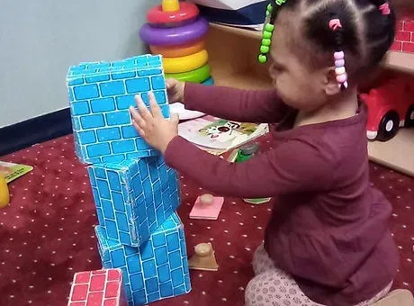 Toddler girl stacking blue toy blocks during guided classroom play